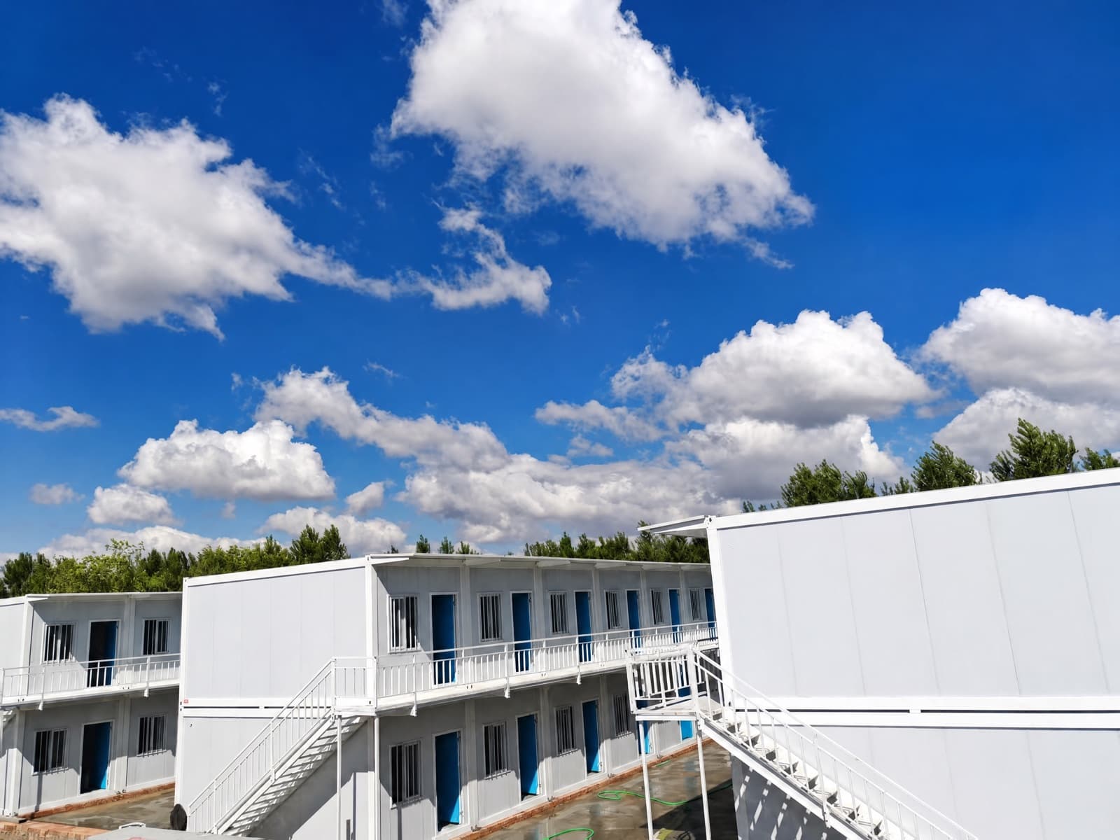 Dãy nhà container hai tầng màu trắng với cửa xanh và cầu thang thép bên ngoài